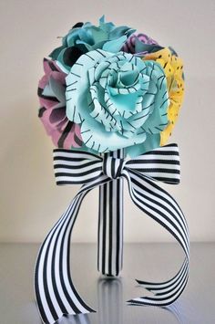 a bouquet of paper flowers in a vase with ribbon tied around the top and bottom