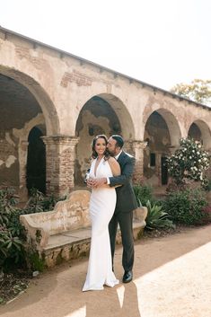 a bride and groom pose for a photo in front of an old building with arches