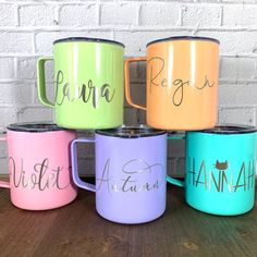 four different colored coffee mugs sitting on top of a wooden table next to a brick wall