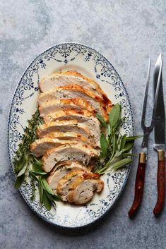 a plate with sliced meat and greens on it next to a pair of knifes