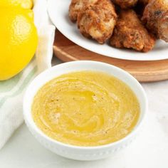 a bowl of dipping sauce next to some fried food on a plate with lemons in the background