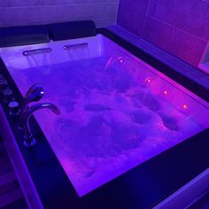 a bathtub filled with water next to a sink under a purple light in a bathroom