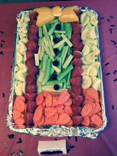 a platter filled with fruits and vegetables on top of a purple cloth covered table