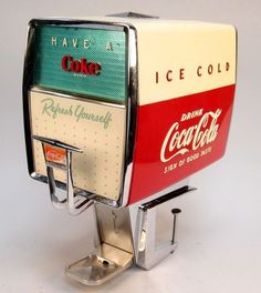 an ice cold drink machine sitting on top of a white table next to a bottle opener