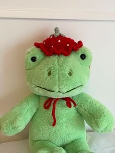 a green frog stuffed animal with a red bow on its head sitting on a white surface