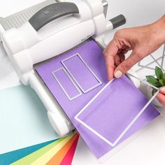 a person cutting paper with a machine on top of it and a plant next to it