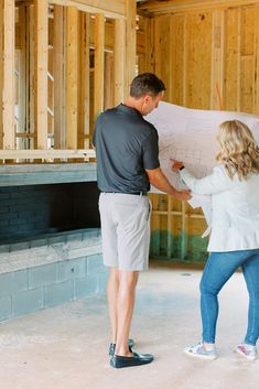 a man and woman looking at blueprint while standing in an unfinished building