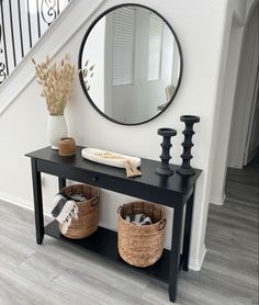 a black console table with two baskets under it and a round mirror on the wall