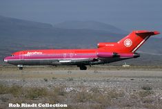 a red and silver airplane is on the tarmac with mountains in the back ground