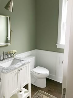 a white toilet sitting next to a bathroom sink under a mirror on top of a wooden floor