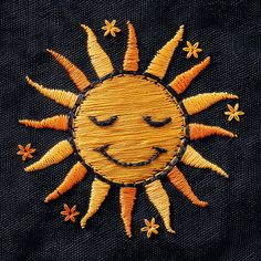 an embroidered sun with eyes and smiling faces on black fabric, close - up photo