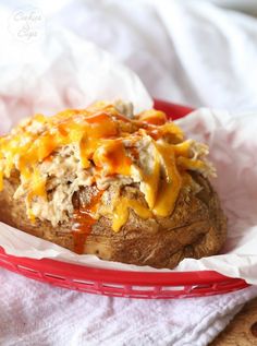 a baked potato covered in cheese and other toppings on a red basket next to a white towel