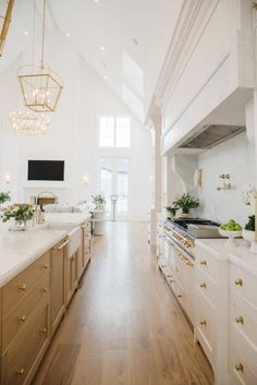 a large kitchen with wooden floors and white walls, along with gold accents on the cabinets