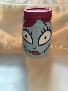 a jar with a painted face on it sitting on a white cloth covered tablecloth