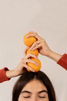 a woman holding an orange up to her head with both hands on top of it