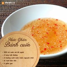 a white bowl filled with liquid next to a wooden sign that says banh cuon