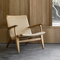 a wooden chair sitting in front of a window next to a wall with wood paneling