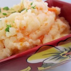 mashed potatoes in a red bowl with green garnish on the top and sides