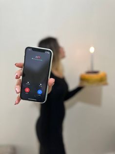 a woman holding up a cell phone in front of a cake with a candle on it