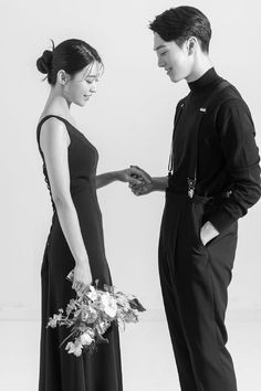 a man and woman standing next to each other in black dresses holding hands with flowers