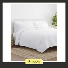 a bed with white sheets and pillows on top of a rug next to a potted plant