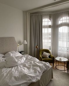 a bed with white sheets and pillows in a bedroom next to a large glass window