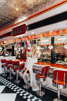 a woman sitting at a diner counter in front of red chairs and neon signs on the ceiling