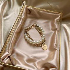 a gold bracelet with pearls and a name tag in a box on a satin surface