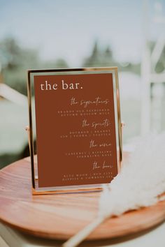 a wooden table topped with a sign next to a white and brown feather on top of it