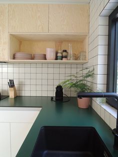 a kitchen with green counter tops and white tile backsplash, black faucet