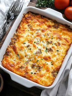 a casserole dish with meat and cheese in it on a wooden table next to tomatoes