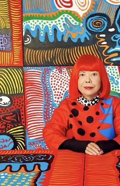 a woman with red hair sitting in front of colorful paintings