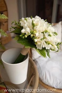 a bouquet of white flowers sitting in a vase on a table next to a bed