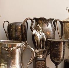 several antique silver cups and vases are on the shelf next to each other, including one with a horse figurine