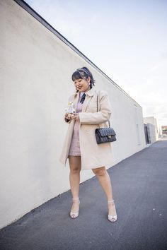 a woman in a trench coat is holding a purse and looking at her cell phone