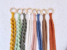 six different colors of crochet keychains hanging on a white background with a wooden ring in the middle