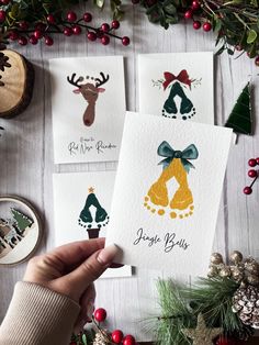 someone holding up some christmas cards on top of a table with other holiday items and decorations