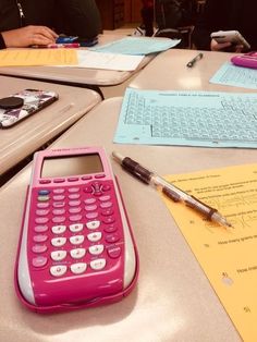 a pink calculator sitting on top of a table next to a pen and paper