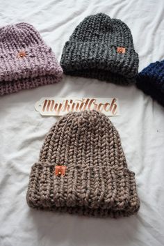 four knitted beanies laid out on a bed