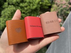 three different colored leather flasks held in someone's hand