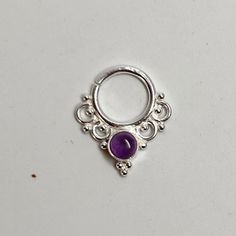 a silver ring with a purple stone in the center on a white surface, next to a pair of scissors