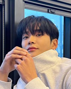 a young man sitting in front of a window with his hand on his chin and looking out the window