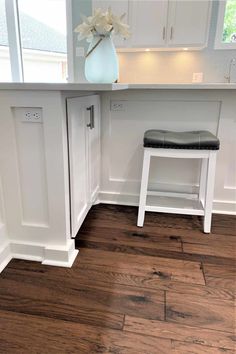 a kitchen with white cabinets and wood flooring on the walls, along with a black leather stool