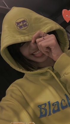 a woman in a yellow hoodie holding her hand up to her face