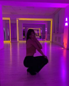 a woman kneeling on the floor in a room with purple lighting and neon lights behind her