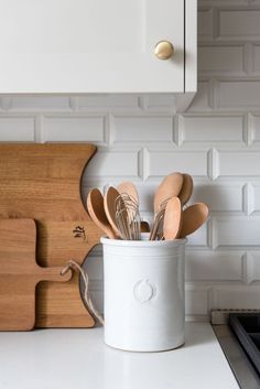 wooden utensils are in a white container on the counter next to a cutting board