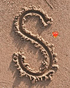 the letter s is drawn in the sand with a red heart on it's side