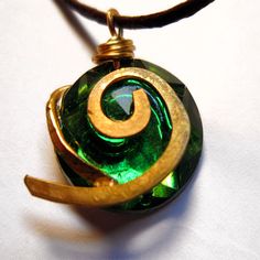 a green and gold necklace with a spiral design on the front, hanging from a leather cord