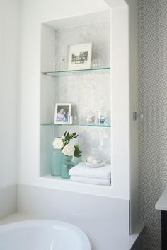 a white bathroom with glass shelves above the bathtub and flowers in vases on the shelf