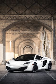 a white sports car is parked in an empty parking lot with arched doorways behind it